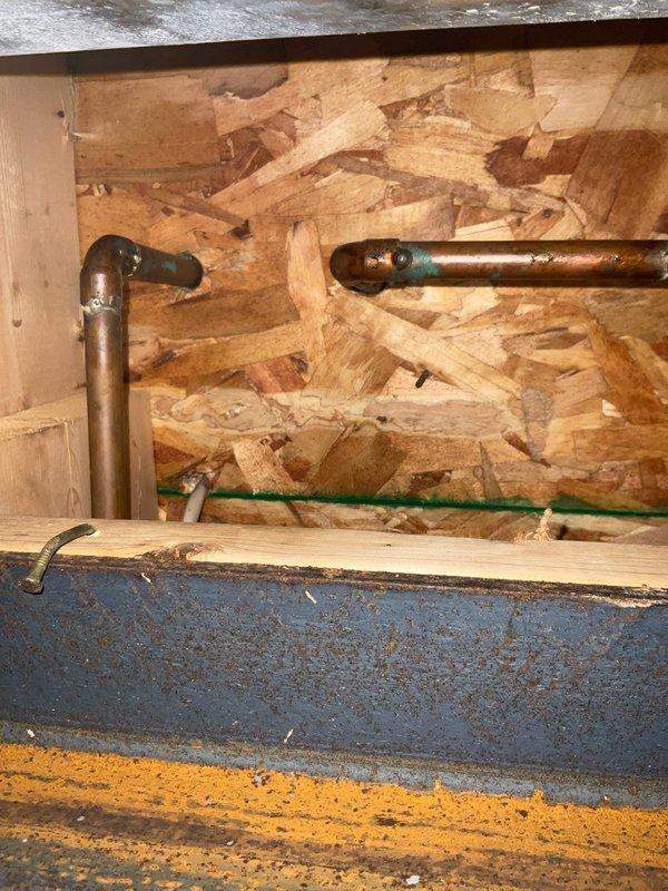 Responded to a first-floor bathroom sink drain leak with water intrusion into the basement. Upon inspection, identified a compromised PVC drain pipe connection at or near the wall penetration point, evidenced by active water staining on the bathroom floor at the pipe base and moisture dripping through to the basement ceiling below. Accessed the affected plumbing from the basement crawl space where the drain line was visible against the OSB wall backing. Repaired the leaking PVC connection, verified proper drainage flow, and confirmed cessation of water intrusion to the basement area.