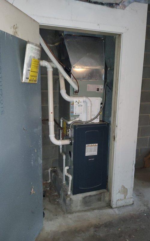 Completed comprehensive maintenance service on residential forced-air heating and cooling system. Performed thorough inspection of indoor furnace unit and air handler located in basement utility area, verified proper operation of all internal components with access panel open for detailed examination. Checked electrical connections, control boards, and safety systems for proper function. Inspected white PVC condensate drain lines and venting system for proper drainage and secure connections. Evaluated outdoor air conditioning condenser unit mounted on concrete pad, assessed refrigerant line set routing and insulation integrity from exterior unit through wall penetration to indoor equipment. Verified electrical disconnect box and power supply connections at outdoor unit. Confirmed proper airflow through condenser coil fins and fan operation. System operating within normal parameters with no immediate repairs required at time of service.