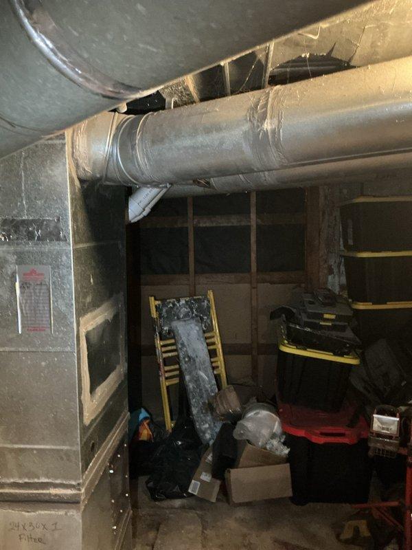 Conducted follow-up inspection of existing basement HVAC installation featuring Carrier furnace system with associated air handler, refrigerant lines, and condensate drainage. Documented current equipment condition and surrounding ductwork infrastructure, noting exposed metal ductwork with partial insulation wrap supported by ceiling-mounted brackets throughout the utility space.