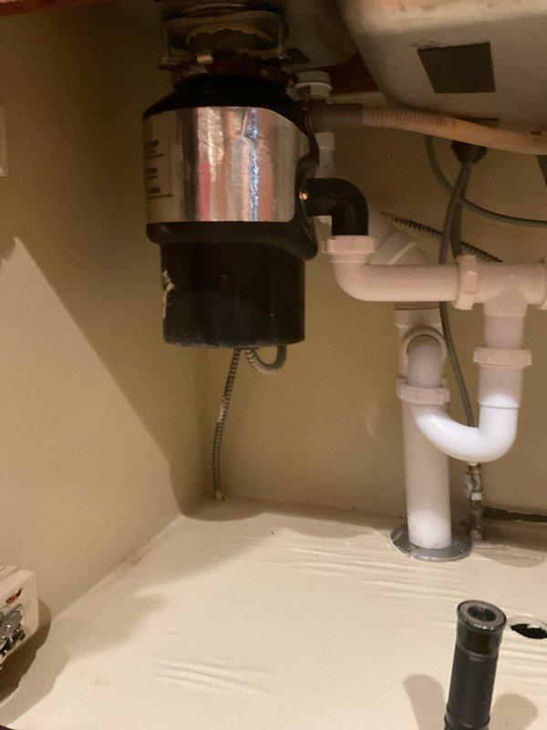Responded to kitchen sink leak in century-old home. Upon inspection, identified deteriorated P-trap connections and worn gaskets beneath sink causing water seepage into cabinet. Disassembled existing white PVC P-trap assembly, inspected garbage disposal connections and drain lines for additional wear. Replaced compromised drain components, installed new P-trap with proper seals, and verified all connections to disposal unit and main drain line were secure and leak-free. Tested system thoroughly under full water flow, confirmed no active leaks, and documented completed repairs with photographs.