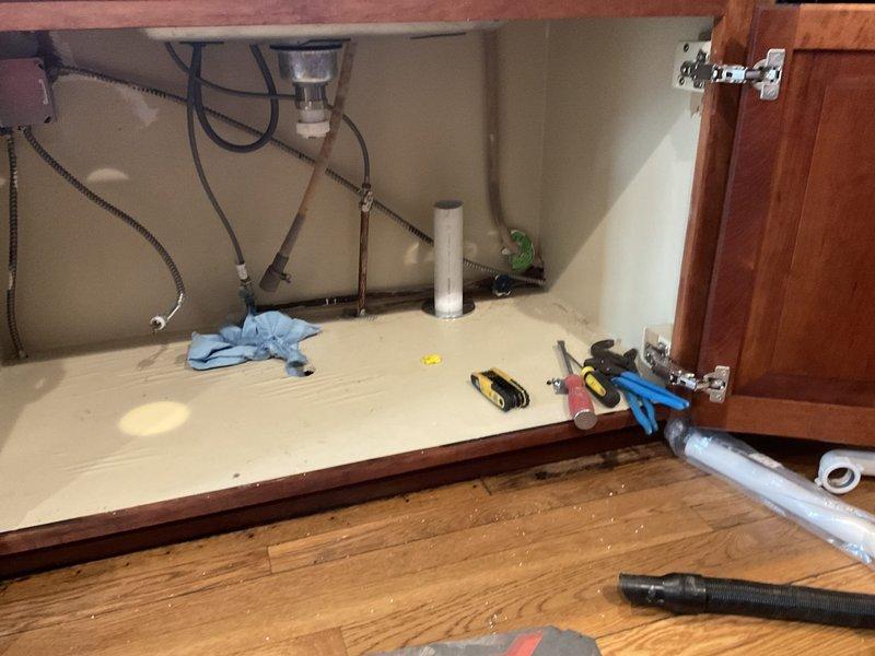 Responded to kitchen sink leak in century-old home. Upon inspection, identified deteriorated P-trap connections and worn gaskets beneath sink causing water seepage into cabinet. Disassembled existing white PVC P-trap assembly, inspected garbage disposal connections and drain lines for additional wear. Replaced compromised drain components, installed new P-trap with proper seals, and verified all connections to disposal unit and main drain line were secure and leak-free. Tested system thoroughly under full water flow, confirmed no active leaks, and documented completed repairs with photographs.