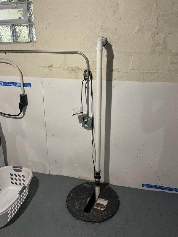 Conducted site evaluation of existing sump pump system in basement utility area to provide estimate for battery backup installation. Assessed current white PVC discharge pipe configuration with vertical run and flexible connector section, noting functional primary pump with black base plate and wall-mounted control components. Identified outdoor spigot requiring permanent capping to prevent water infiltration. Documented significant water damage and staining on interior door and wall surfaces near entry point, indicating historical moisture intrusion issues that necessitate proper exterior penetration sealing when spigot is capped off.