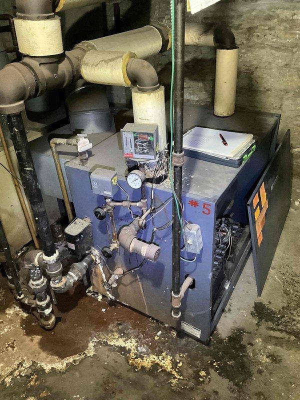 Conducted on-site boiler assessment at commercial funeral home facility. Evaluated existing boiler unit #5 and associated mechanical systems in basement mechanical room. Documented equipment condition, piping configuration, insulated supply lines, pressure gauges, and valve assemblies. Observed floor staining and moisture indicators around unit base suggesting potential historical leakage or condensate issues. Photographed current installation setup including connections, fittings, and surrounding infrastructure to support estimate preparation for equipment replacement or system upgrades.