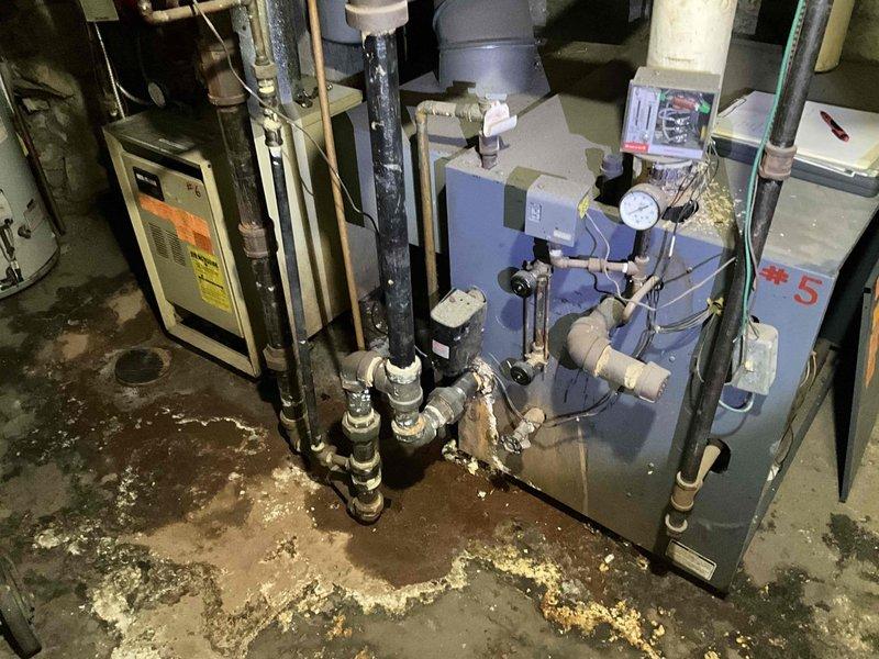Conducted on-site boiler assessment at commercial funeral home facility. Evaluated existing boiler unit #5 and associated mechanical systems in basement mechanical room. Documented equipment condition, piping configuration, insulated supply lines, pressure gauges, and valve assemblies. Observed floor staining and moisture indicators around unit base suggesting potential historical leakage or condensate issues. Photographed current installation setup including connections, fittings, and surrounding infrastructure to support estimate preparation for equipment replacement or system upgrades.