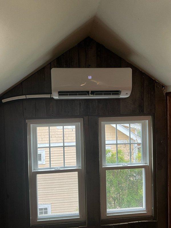 Installed 12,000 BTU one-to-one heat pump mini split system on third floor with indoor head unit mounted above window near ceiling peak. Ran approximately 50-foot line set through line hide concealment, entering below window level and routing up wall to connect to unit. Connected system to dedicated 20-amp circuit from newly installed subpanel, with outdoor condenser mounted on exterior wall and all refrigerant lines and electrical wiring properly secured and protected through white corrugated conduit.