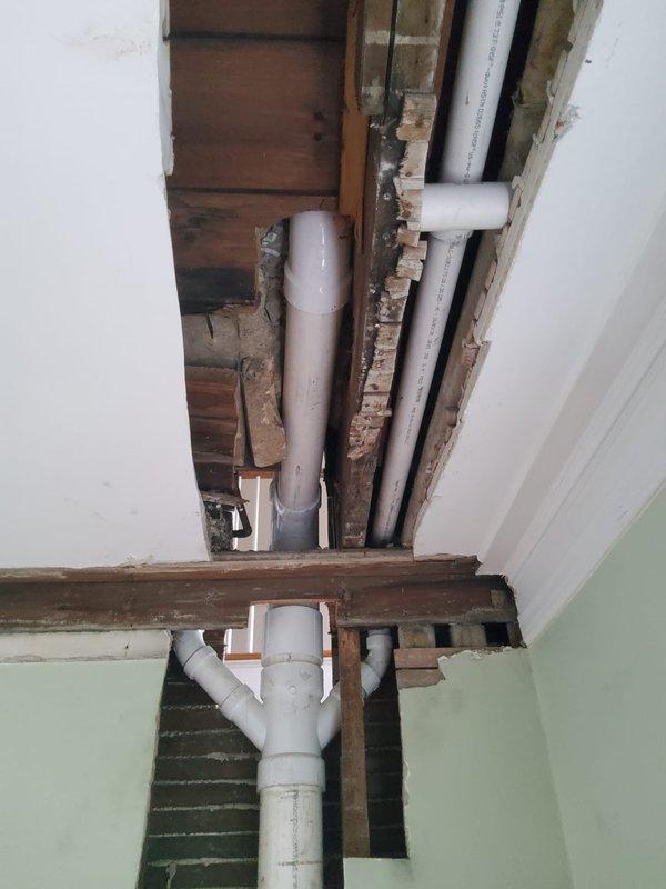 Opened wall in staircase and ceiling in family room to access and expose defective toilet bend. Removed old plumbing components and replaced toilet bend with new PVC piping, extending replacement down through the stack to basement floor level. Installed new first floor toilet bend and tied connection onto existing sink drain line using PVC Y-fitting. Replaced old-style 14-inch rough-in toilet on first floor due to incompatibility with updated plumbing configuration. All new drain and vent piping installed to code specifications with proper slope and connections secured throughout vertical stack system.