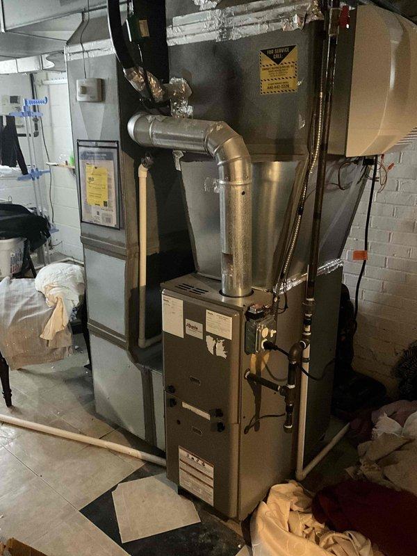 Conducted on-site assessment for complete furnace and air conditioning system replacement. Evaluated existing basement HVAC installation including current furnace unit, air handler, and associated ductwork system. Documented equipment specifications, existing infrastructure conditions, and spatial requirements for new system installation. Photographed current setup showing beige furnace with metallic ductwork, adjacent air handler, copper refrigerant lines, and branch duct configuration. Noted wall conditions and provided comprehensive replacement estimate for new heating and cooling equipment.