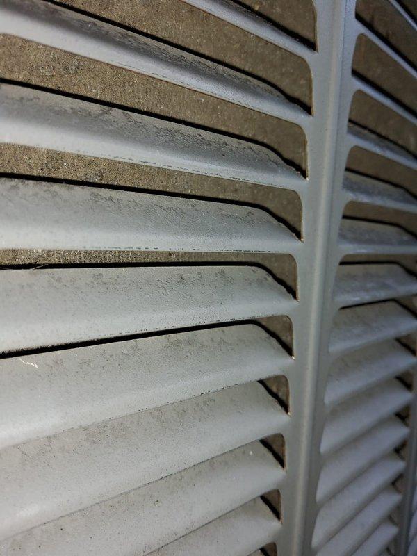 Responded to no-cooling complaint where indoor unit failed to reduce temperature. Upon arrival, found outdoor AC unit not operating. Inspection revealed condenser unit with significant dust and debris accumulation on ventilation louvers and grilles, restricting airflow. White frost-like substance and heavy contamination observed on multiple horizontal slats of exterior grilles, particularly concentrated on upper portions of unit. Documented condition of equipment with photos showing extent of buildup on both darker and lighter-colored ventilation components. The accumulated material on louver surfaces and compromised airflow indicated maintenance neglect contributing to system failure.