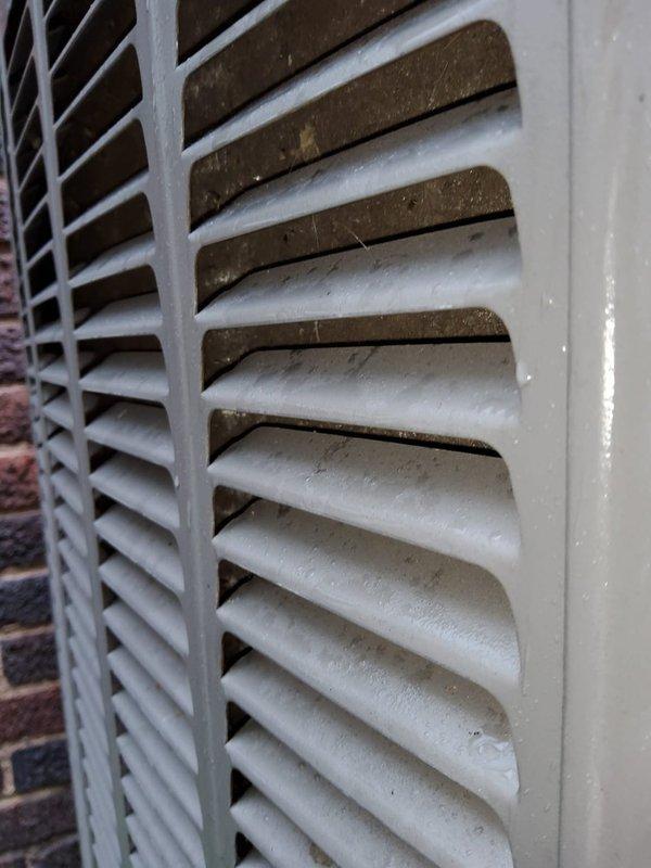 Responded to no-cooling complaint where indoor unit failed to reduce temperature. Upon arrival, found outdoor AC unit not operating. Inspection revealed condenser unit with significant dust and debris accumulation on ventilation louvers and grilles, restricting airflow. White frost-like substance and heavy contamination observed on multiple horizontal slats of exterior grilles, particularly concentrated on upper portions of unit. Documented condition of equipment with photos showing extent of buildup on both darker and lighter-colored ventilation components. The accumulated material on louver surfaces and compromised airflow indicated maintenance neglect contributing to system failure.