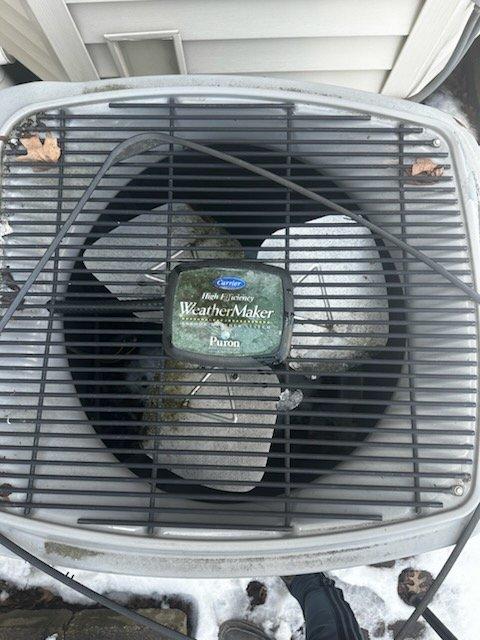 Responded to insurance diagnostic request for 20-year-old Carrier WeatherMaker Infinity air conditioning system reportedly damaged by falling ice block. Performed visual inspection and photographic documentation of outdoor condenser unit, noting weathered condition consistent with age, accumulated debris on fan grille, and rust spots on casing and corners. Assessed top-mounted fan assembly, grille integrity, and motor housing for impact damage, documenting findings for insurance claim purposes.
