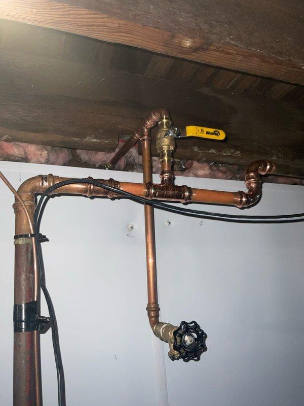 Responded to plumbing service call at century-old residential property for pipe repair assessment. Upon arrival, inspected exposed copper plumbing infrastructure in basement/utility area with accessible ceiling joists and insulation. Evaluated aging copper pipe system showing natural oxidation and patina consistent with older installation. Verified all shut-off valves, including yellow-handled ball valve and black wheel-style valve, were operational and properly functioning. Confirmed water supply remained active with no active leaks or water damage present at time of inspection. Documented existing plumbing configuration including multiple pipe joints, elbows, brass fittings, and connection points throughout the assembly. Assessed overall system integrity and identified areas requiring monitoring due to age-related wear on copper piping.