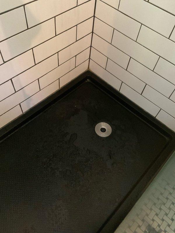 Responded to a clogged shower drain in a 110-year-old residential property. Upon arrival, assessed the black textured shower pan with center brass drain fixture and determined the blockage was preventing proper drainage. Cleared the obstruction using appropriate drain clearing tools and techniques, restoring full water flow through the drain system. Tested the drain thoroughly to ensure complete functionality and documented the completed work with photographs of the shower base and surrounding white subway tile installation.