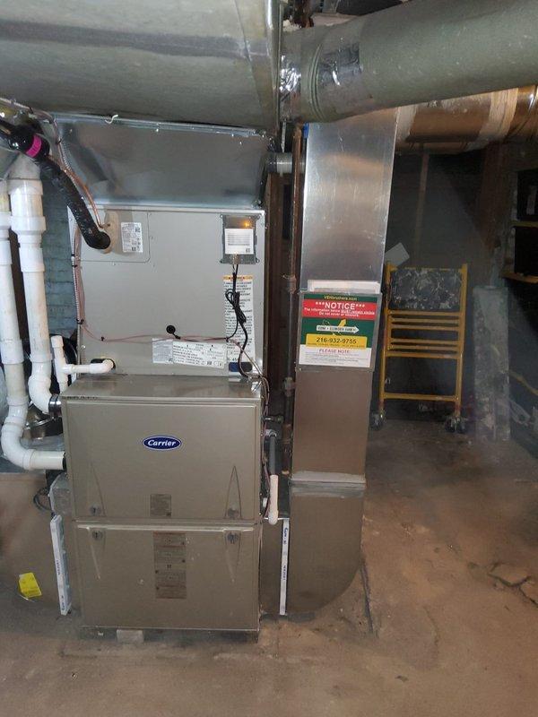 Completed add-on air conditioning installation to existing forced-air heating system. Disconnected and repositioned existing Carrier furnace, rerouted return air ducting to draw from both sides of unit to accommodate new evaporator coil mounted on top of furnace. Installed outdoor condenser unit at rear of property with refrigerant line set, electrical disconnect, and PVC conduit for power supply connection. Evaluated second-floor bathroom airflow concerns and provided recommendations for improved duct distribution. System ready for final electrical connection by outside contractor.