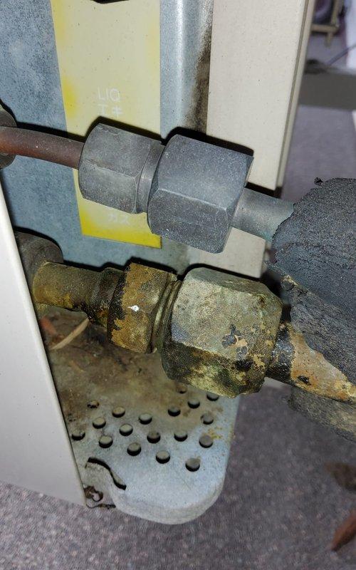 Responded to service call for air conditioning system not blowing cold air. Upon inspection, discovered severely corroded refrigerant line connections at the air handler unit located in the attic space. The compression fittings and coupling nuts exhibited heavy oxidation with greenish-brown patina, indicating prolonged moisture exposure and compromised refrigerant line integrity. Documented the corroded connections and overall system condition with photographic evidence. The deteriorated fittings pose a potential refrigerant leak risk that requires immediate attention to restore proper cooling function and system efficiency.