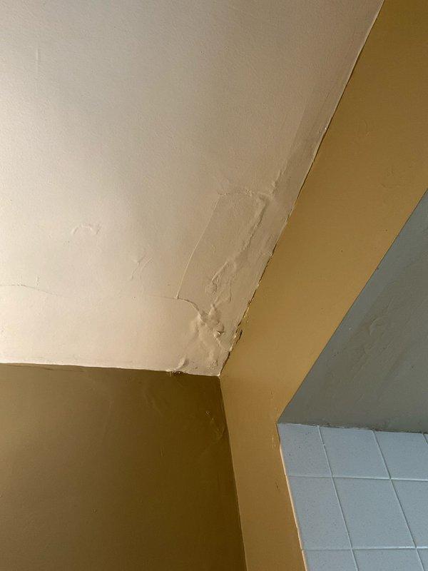 # Plumbing Service - Water Leak

Responded to reported water leak concern in downstairs unit of 1920s-era duplex. Upon arrival, conducted thorough visual inspection of interior spaces to identify source and extent of moisture intrusion.

## Findings and Assessment

Discovered active water damage in bathroom ceiling area with prominent brown staining and discoloration indicating ongoing or recent moisture infiltration. Ceiling surface displayed multiple areas of water damage with diagonal staining patterns and darker patches consistent with water migration through ceiling materials. Identified additional deterioration at wall-to-ceiling corner joint showing compromised plaster/drywall compound with rough, uneven texture and raised surface irregularities.

Damage patterns suggest water source originating from plumbing system or fixtures in unit above. Moisture penetration has compromised ceiling integrity and corner seam structural finish. Tile work and lower wall sections remain intact 