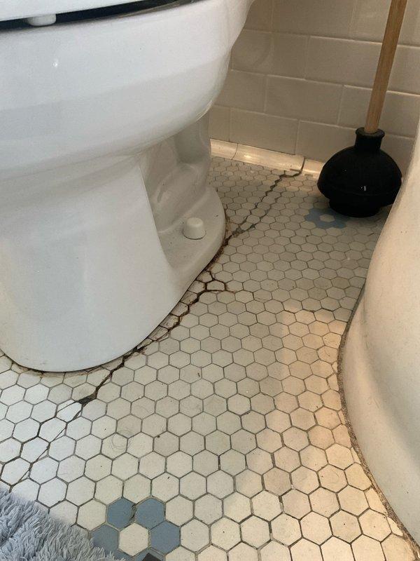 Responded to service call for second floor toilet with water leaking from base. Upon inspection, found 14-year-old toilet with failed wax ring seal causing water seepage at floor junction. Evidence of long-term moisture damage visible in grout lines and discoloration around toilet base on hexagonal tile flooring. Removed and reset toilet, replaced deteriorated wax seal with new wax ring, ensured proper flange connection, and reinstalled toilet with secure mounting. Verified watertight seal at base and confirmed no active leaks during testing.