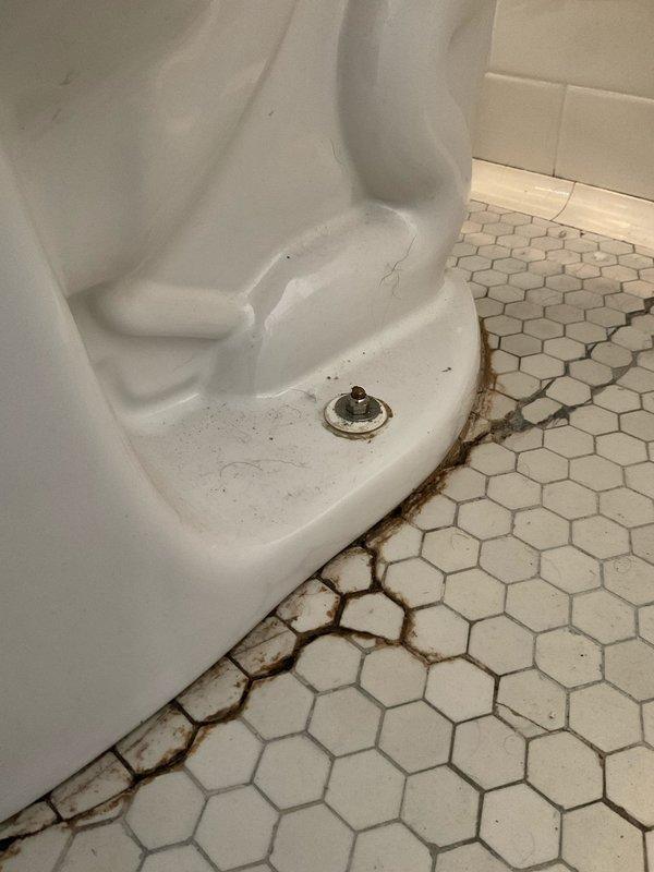 Responded to service call for second floor toilet with water leaking from base. Upon inspection, found 14-year-old toilet with failed wax ring seal causing water seepage at floor junction. Evidence of long-term moisture damage visible in grout lines and discoloration around toilet base on hexagonal tile flooring. Removed and reset toilet, replaced deteriorated wax seal with new wax ring, ensured proper flange connection, and reinstalled toilet with secure mounting. Verified watertight seal at base and confirmed no active leaks during testing.