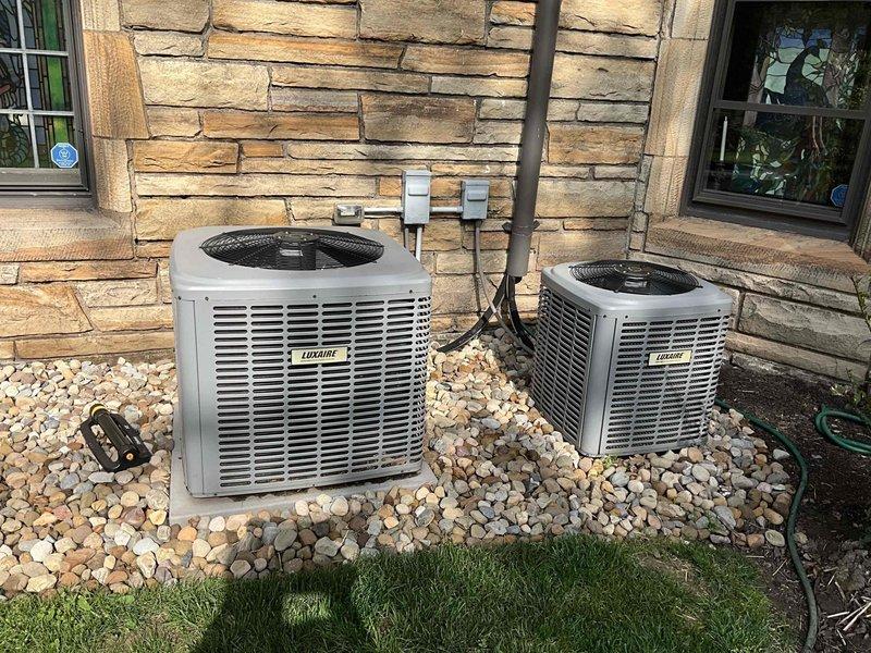 # HVAC System Replacement - Dual Unico Mini Split Installation

Completed replacement of two Unico system units serving the east wing and west wing of the residence. Accessed attic space using 8-foot frame ladder to remove existing air handler equipment and associated ductwork. Installed new beige air handler units in attic, positioning them on insulated attic floor among existing rafters and maintaining proper clearances from flexible ductwork runs.

Exterior work included installation of two Luxaire outdoor condensing units positioned side by side on stone facade wall. Units were mounted on river rock bed with appropriate spacing for service access and airflow. Ran electrical conduit and refrigerant line sets between outdoor units and attic-mounted air handlers, securing all connections per manufacturer specifications. Completed electrical connections with junction boxes mounted to exterior wall between units.

System tested and confirmed operational for both east and west wing zones