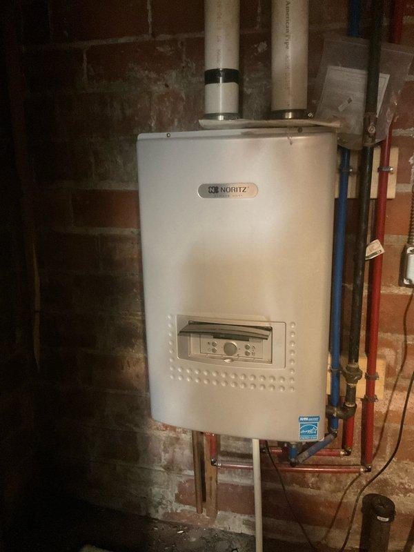 Responded to service call for leaking Noritz tankless water heater in 100-year-old home. Inspected wall-mounted unit and associated plumbing connections, including copper supply lines, PEX distribution manifold, and PVC venting system. Evaluated multiple shut-off valves, brass fittings, and complex pipe routing to identify source of leak and assess overall system condition in aged basement environment with exposed masonry walls.
