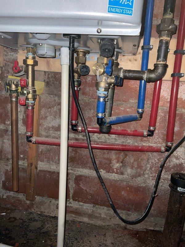 Responded to service call for leaking Noritz tankless water heater in 100-year-old home. Inspected wall-mounted unit and associated plumbing connections, including copper supply lines, PEX distribution manifold, and PVC venting system. Evaluated multiple shut-off valves, brass fittings, and complex pipe routing to identify source of leak and assess overall system condition in aged basement environment with exposed masonry walls.