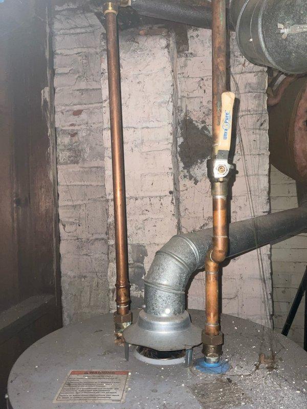 Responded to service call for leaking tanked water heater in basement utility area. Upon inspection, assessed the existing water heater installation including copper supply lines, brass compression fittings, and connection points for signs of active leakage and deterioration. Examined the tank unit, plumbing connections, temperature and pressure relief valve, and surrounding pipe infrastructure to determine source of leak and evaluate overall system condition. Documented existing conditions with photographs showing aged copper piping with natural patina, galvanized fittings, and deteriorated basement environment. Provided customer with assessment findings and presented options for both repair solutions and full water heater replacement based on the severity of the leak and age of the existing equipment.