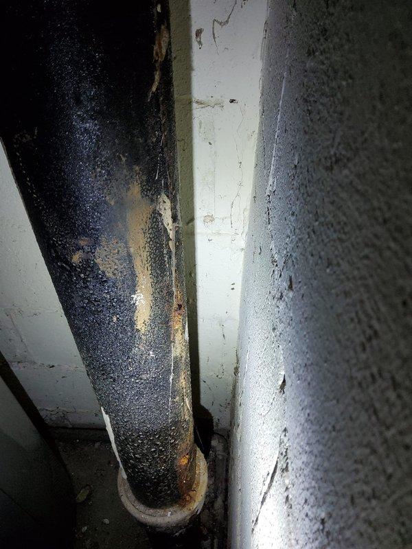 Completed comprehensive plumbing assessment of utility area as requested. Inspection revealed extensive corrosion and deterioration on vertical metal supply piping, with significant rust staining and surface degradation requiring attention. Documented mixed-age plumbing installation featuring corroded metal components connected to newer PVC piping via rubber coupling sleeves, along with moisture exposure affecting adjacent ductwork and mechanical components.