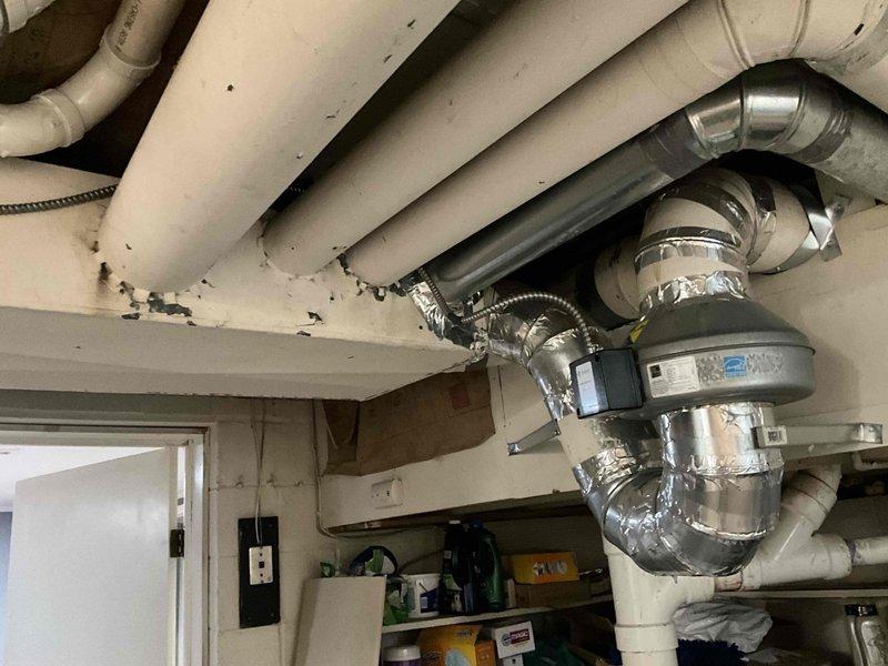 Conducted on-site evaluation for boiler system installation or replacement. Assessed existing HVAC infrastructure including exposed ductwork, ventilation components, and exhaust venting in utility area with cinder block construction. Documented current mechanical system configuration, duct connections, and venting pathways to determine optimal boiler placement and integration requirements. Photographed existing conditions including overhead ductwork arrangements, PVC plumbing lines, and horizontal exhaust vent penetrations through exterior wall to provide accurate basis for equipment sizing and installation planning.