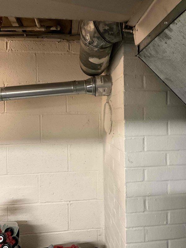Conducted on-site evaluation for boiler system installation or replacement. Assessed existing HVAC infrastructure including exposed ductwork, ventilation components, and exhaust venting in utility area with cinder block construction. Documented current mechanical system configuration, duct connections, and venting pathways to determine optimal boiler placement and integration requirements. Photographed existing conditions including overhead ductwork arrangements, PVC plumbing lines, and horizontal exhaust vent penetrations through exterior wall to provide accurate basis for equipment sizing and installation planning.