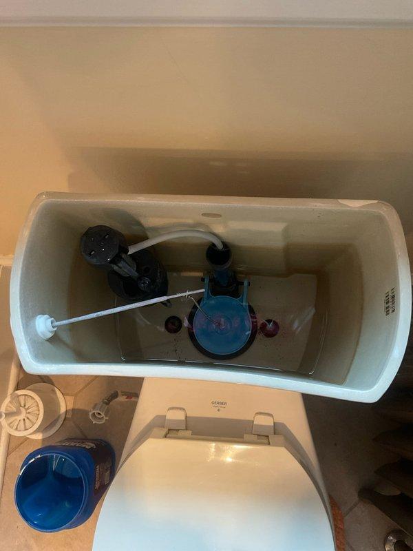Responded to complaint of toilet slow to fill after flushing in 100-year-old residence. Upon inspection, removed tank lid and evaluated internal flush mechanism components. Identified aging fill valve assembly with standard float ball configuration as source of reduced flow rate. Inspected flush valve, flapper, and overflow tube assembly for proper operation. All components showed signs of age-consistent mineral deposits and wear. Tested fill valve operation through multiple flush cycles to confirm slow fill condition. Documented existing blue fill valve mechanism and black flush valve assembly with photographic evidence for service records. Recommended fill valve replacement to restore proper fill time and water flow efficiency.