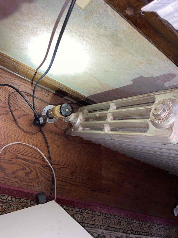 Responded to service call for steam radiator system with multiple radiators lacking proper vents. Inspected basement heating units and identified several cast iron radiators without functioning air vents, preventing proper steam circulation and heat distribution. Observed significant calcium buildup on main control valve affecting hot/cold water regulation. Documented conditions with photos showing aged radiator components with rust deterioration and worn paint surfaces. Provided estimate for drilling and tapping radiator bodies to install new air vents, which will allow trapped air to escape and enable proper steam heating operation throughout the system.