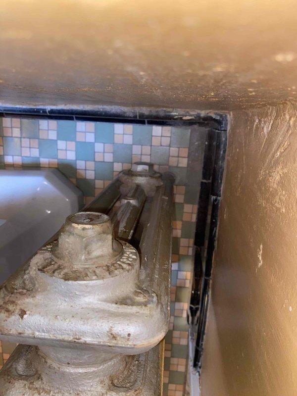 Responded to service call for steam radiator system with multiple radiators lacking proper vents. Inspected basement heating units and identified several cast iron radiators without functioning air vents, preventing proper steam circulation and heat distribution. Observed significant calcium buildup on main control valve affecting hot/cold water regulation. Documented conditions with photos showing aged radiator components with rust deterioration and worn paint surfaces. Provided estimate for drilling and tapping radiator bodies to install new air vents, which will allow trapped air to escape and enable proper steam heating operation throughout the system.