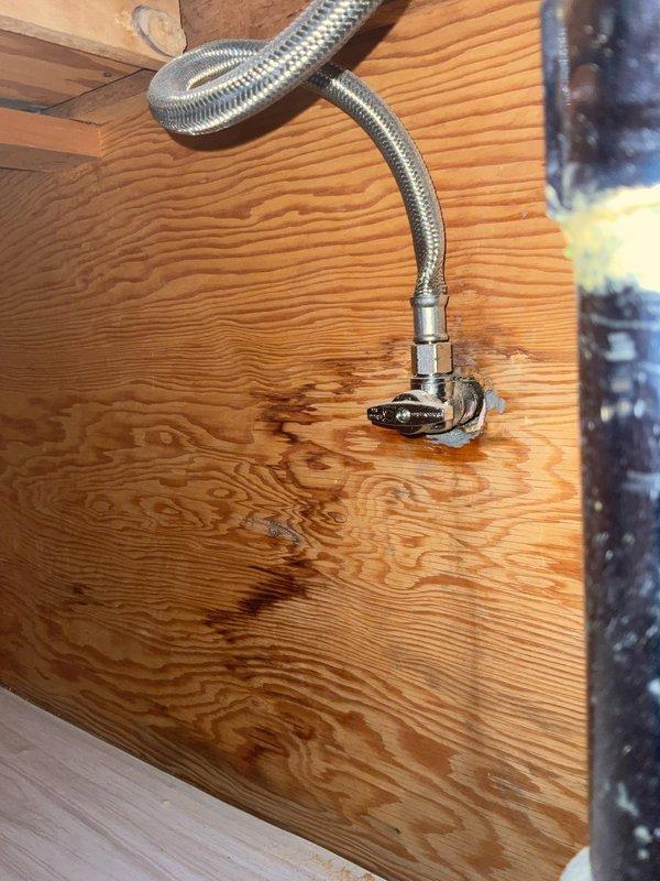 Installed water supply line components through floor access opening, including 2 3/8" threaded angle stop valve and 1/2" compression fitting. Connected flexible braided metal supply hose to brass fittings using two 3/8" brass nipples of varying lengths (4"-6") to complete the water supply connection. All connections were secured and tested for proper operation.