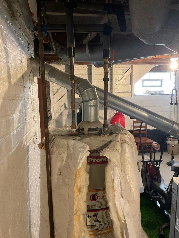 Responded to call regarding water heater backdrafting and gas odor occurring when AC system activates. Inspected A.O. Smith 40-gallon natural gas water heater (Model GCV 40 100, 40,000 BTU input) and shared venting system with HVAC equipment. Evaluated chimney draft conditions, venting configuration, and combustion air supply to diagnose backdrafting issue caused by negative pressure when air conditioning system operates. Documented existing installation conditions including spray foam insulation on tank, copper supply piping, and shared flue arrangement with photographic evidence for further assessment and recommended corrective actions to resolve unsafe venting condition.
