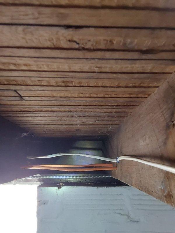 Conducted site assessment for dryer vent installation through existing glass block window in utility area. Evaluated structural conditions including deteriorated wooden window frame and exposed ceiling joists with existing electrical wiring running through cavity. Documented current conditions and photographed installation location to determine appropriate venting solution and materials needed for future dryer exhaust system installation.