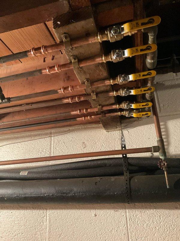 Removed six existing multi-turn shut-off valves from the basement plumbing manifold system and replaced them with new ProPress ball valves featuring yellow lever handles. The new valves were oriented with proper spacing and positioning to allow easy operation without interference between adjacent handles, improving accessibility and functionality of the copper pipe distribution system mounted on the concrete block wall.