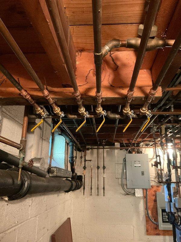 Removed six existing multi-turn shut-off valves from the basement plumbing manifold system and replaced them with new ProPress ball valves featuring yellow lever handles. The new valves were oriented with proper spacing and positioning to allow easy operation without interference between adjacent handles, improving accessibility and functionality of the copper pipe distribution system mounted on the concrete block wall.