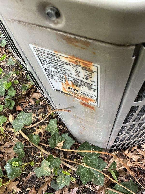 Conducted on-site evaluation of 13-year-old residential HVAC system for replacement estimate. Assessed outdoor condensing unit showing significant age-related deterioration, including rust streaking, corrosion around mounting hardware, and weathered housing. Noted unit installed on ground with leaf debris and vegetation growth rather than proper concrete pad. Inspected indoor equipment including furnace and air handler in basement location. Documented existing system configuration with connected ductwork and control components. Photographed equipment condition and installation details to support replacement recommendation.