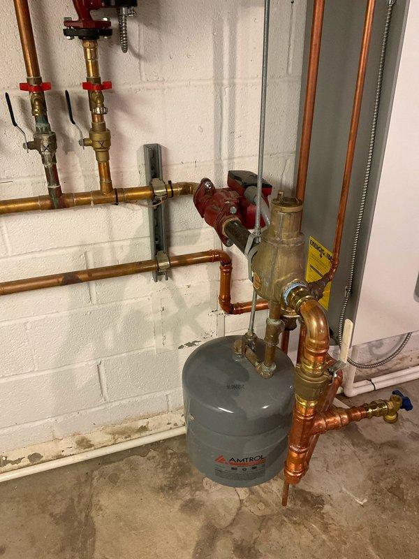 Responded to service call for water heater repair at residential property with 2-year-old Triangle Tube system. Upon inspection, verified proper operation of hydronic heating unit and associated components including expansion tank, copper supply lines, pressure relief valves, and zone control valves. System showed normal operating parameters with expansion tank maintaining appropriate pressure and all shut-off valves functioning correctly. Documented existing installation configuration including PVC condensate drainage, flexible metallic conduit connections, and brass valve assemblies with red handles for system isolation and maintenance access.