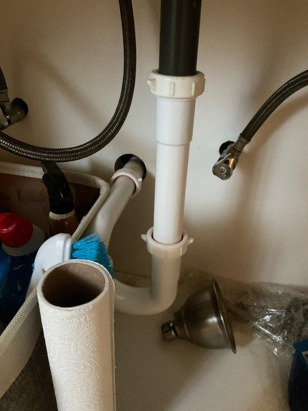 Responded to clogged drain issue in bathroom sink of century-old home with recent remodel. Upon inspection, identified blockage in drain line and observed rust-colored staining around drain opening indicating possible mineral buildup or deteriorating components. Accessed P-trap assembly beneath sink through vanity cabinet, which featured white PVC slip-joint configuration connected to vertical drain pipe. Disassembled P-trap sections to clear obstruction and remove accumulated debris. Inspected all drain components for proper alignment and secure connections. Cleaned trap sections and reassembled plumbing system, ensuring all slip-joint fittings were properly tightened to prevent future leaks. Tested drain flow with running water to verify complete clearance and proper drainage. System restored to full functionality with no leaks detected at connections.