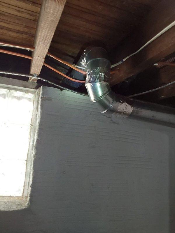 Installed new dryer vent system routing from interior laundry area through exterior wall. Ran rigid metallic ductwork through basement ceiling joists, secured with appropriate fasteners and sealed all connections with aluminum foil tape to ensure airtight installation. Mounted exterior vent termination hood with damper on cream-colored siding above brick foundation, completing penetration through wall and ensuring proper clearance from existing copper plumbing lines and utilities.