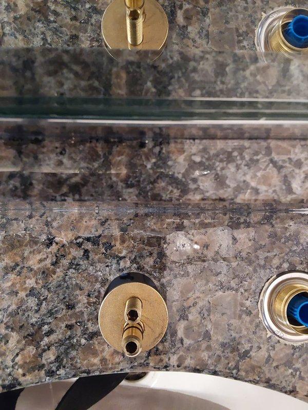 Completed installation of brass wall-mounted faucet valves and fixtures on bathroom vanity with granite countertop. Installed escutcheon plates, valve stems, and connected chrome supply lines to ensure proper water flow to sink basin. All fixtures secured and tested for functionality.
