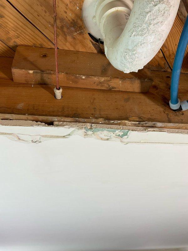 Responded to contractor concern regarding plumbing fixtures hanging below ceiling rafters preventing drywall installation. Assessed exposed 2" PVC drain line and trap configuration in attic space that was improperly positioned below structural beams. Documented existing conditions showing white plumbing fixtures, drain piping, and various mechanical lines running through ceiling joists. Provided consultation on proper installation methods to reconfigure drain assembly within rafter depth to allow for ceiling finish work to proceed.