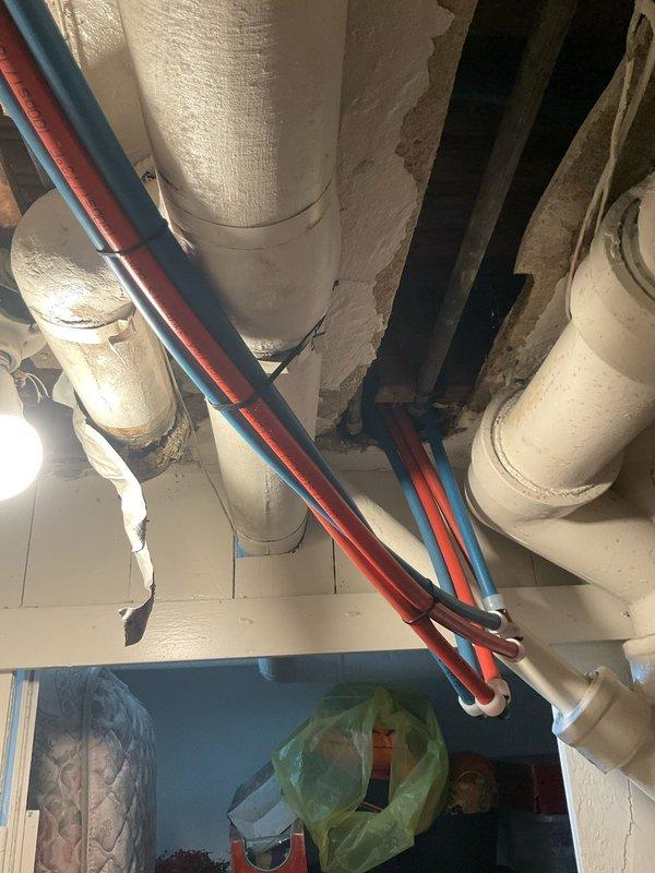 Responded to contractor concern regarding plumbing fixtures hanging below ceiling rafters preventing drywall installation. Assessed exposed 2" PVC drain line and trap configuration in attic space that was improperly positioned below structural beams. Documented existing conditions showing white plumbing fixtures, drain piping, and various mechanical lines running through ceiling joists. Provided consultation on proper installation methods to reconfigure drain assembly within rafter depth to allow for ceiling finish work to proceed.