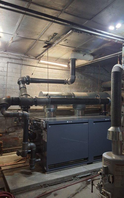 Completed full steam boiler replacement in commercial mechanical room, including removal of existing unit and installation of dual dark blue commercial-grade steam boilers positioned on concrete platform. Replaced boiler feed pump and feeder system with new equipment. Reconnected all supply and return steam lines using large-diameter black pipe with proper pitch and support, including horizontal distribution mains and vertical risers. Installed new copper piping network with appropriate valves, fittings, and pressure relief devices. Tested all connections for leaks, verified proper operation of feed system, and confirmed steam distribution to existing building infrastructure.
