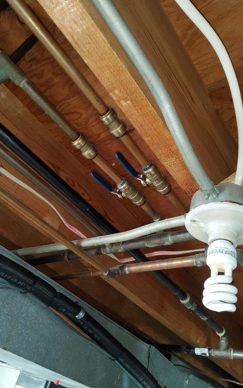 Responded to water leak call in HVAC system. Upon arrival, inspected basement plumbing infrastructure and located leak at copper pipe junction with compression fitting near blue-handled ball valve. Found moisture damage on wooden joists and identified compromised seal at brass fitting connection point. Tightened compression fittings, replaced worn ferrule, and tested all connections under pressure. Inspected adjacent PEX tubing, copper lines, and galvanized piping for additional leak sources. Verified water filtration system and pressure tank mounting were secure and not contributing to moisture issues. Cycled system multiple times to confirm repair integrity and no further leakage detected.