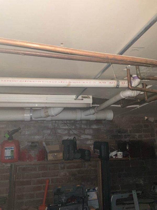 Responded to complaint of toilets gurgling into business below when flushed, with fixtures eventually losing ability to flush properly. Performed diagnostic inspection of plumbing system, focusing on drain and vent lines serving the affected toilets. Inspected exposed drainage piping in basement utility area, examining PVC drain lines, copper water supply lines, and venting configuration. Identified potential drainage obstruction or venting issue affecting proper waste evacuation from upper-level toilet fixtures. Documented existing plumbing infrastructure conditions with photographs showing pipe routing, support systems, and overall basement utility space configuration for further evaluation and repair recommendations.