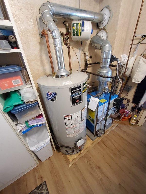 Responded to service call for non-functional tanked water heater with reported gas leak and occasional "snowing" condition in 70-year-old residence. Upon arrival, inspected the white cylindrical water heater unit and surrounding plumbing connections, including copper piping, brass fittings, galvanized ductwork, and expansion tank assembly. Documented existing installation configuration showing multiple pipe connections at top of unit, adjacent blue water treatment system, and utility room conditions. Due to safety concerns regarding the reported gas leak, further diagnostics and corrective action were required to address both the operational failure and hazardous gas condition.