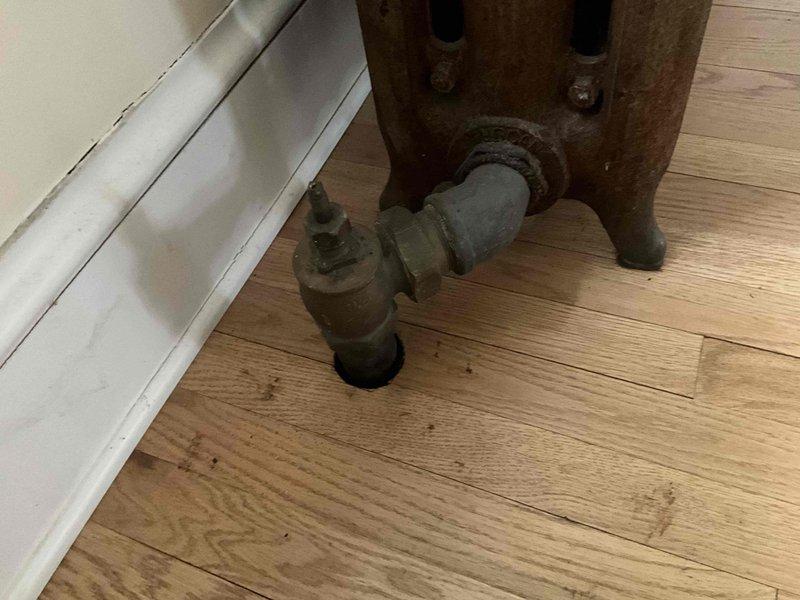 Conducted on-site estimate for living room cast iron radiator replacement or removal and thermostat upgrade. Assessed existing antique cast iron radiator unit showing age-related corrosion and oxidation, along with current circular wall-mounted thermostat. Discussed heating system options and modern thermostat alternatives with customer to determine preferred solution for improved climate control.