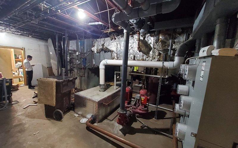 Responded to no-cooling call for 10+ year old air conditioning system located in basement serving first floor. Upon inspection, found aging A/C unit with visible wear and operational issues. Evaluated electrical components including capacitor, examined refrigerant lines and copper piping connections, and assessed overall system functionality. Documented equipment condition and mechanical room setup including ductwork, electrical panels, and ventilation components for diagnostic and repair recommendations.