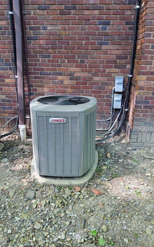 Responded to service call for 15-year-old Lennox air conditioning system. Upon arrival, performed visual inspection of outdoor condenser unit and surrounding components. Discovered damaged electrical wiring with exposed conductors near the unit, including compromised insulation jacket revealing internal green and red wires with exposed copper strands. The damaged wire was found lying across deteriorated cardboard material in the gravel base area, presenting a safety hazard and potential cause of system malfunction.

Inspected electrical disconnect box and conduit connections mounted on exterior brick wall. Assessed the condition of the cylindrical condenser unit with horizontal louvers and top-mounted fan grille. Documented the compromised wiring condition and deteriorated materials around the unit base that could impact electrical safety and system performance. 

Addressed the electrical hazard and restored safe operating conditions to the system. Verified proper connections at the di